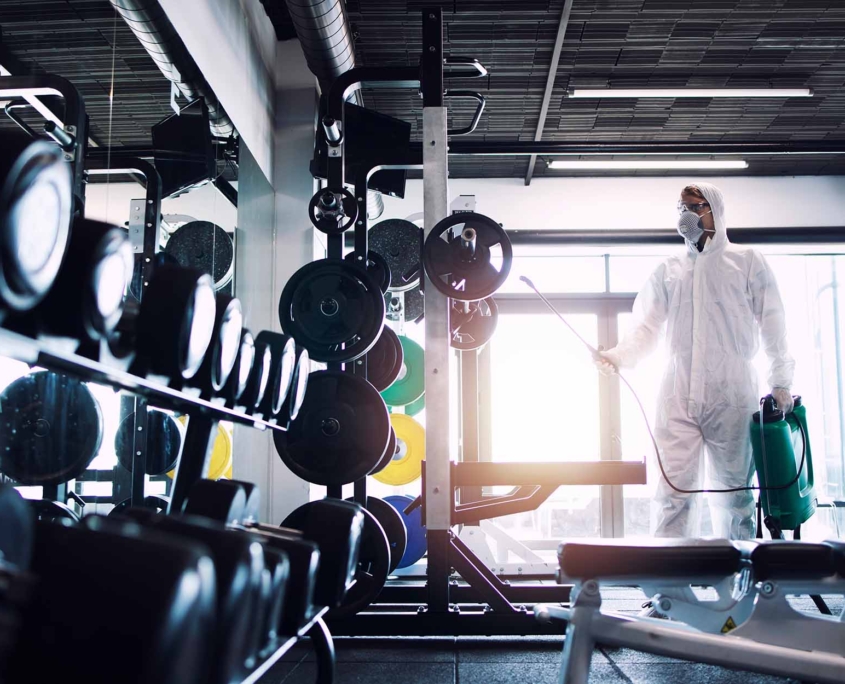 Gym disinfection and healthcare. Man in white protection suit disinfecting and fitness equipment